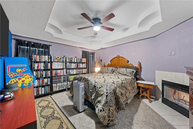 tiled bedroom with ceiling fan, a textured ceiling, a tile fireplace, and a tray ceiling