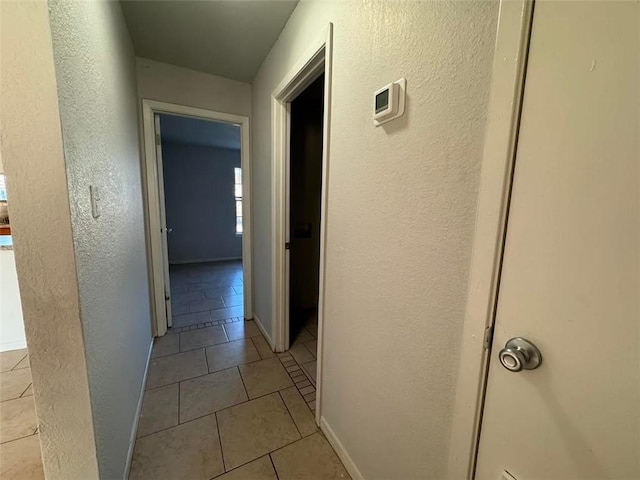 corridor with light tile patterned floors, a textured wall, and baseboards