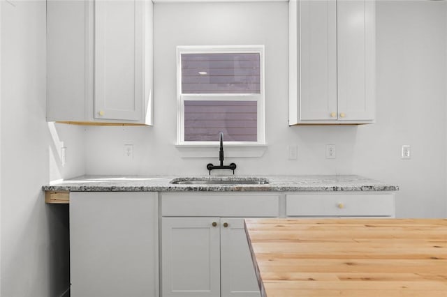 kitchen with white cabinets, a sink, and light stone countertops