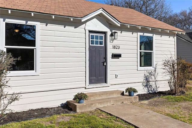 view of exterior entry with roof with shingles