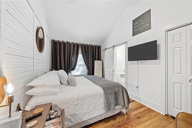 bedroom with a barn door, wood-type flooring, and vaulted ceiling