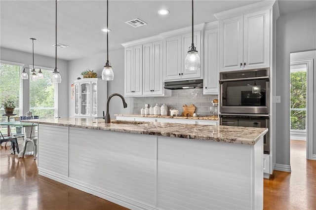 kitchen featuring light stone countertops, concrete flooring, sink, decorative light fixtures, and white cabinetry