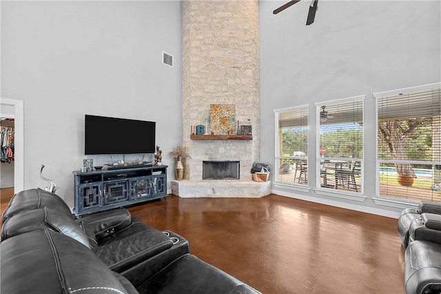 living room with a towering ceiling, a stone fireplace, plenty of natural light, and ceiling fan