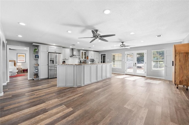 kitchen featuring light stone countertops, wall chimney exhaust hood, dark hardwood / wood-style flooring, stainless steel refrigerator with ice dispenser, and a kitchen island with sink