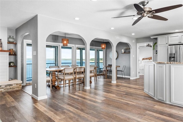 dining room featuring dark hardwood / wood-style floors, ceiling fan, a water view, and a fireplace