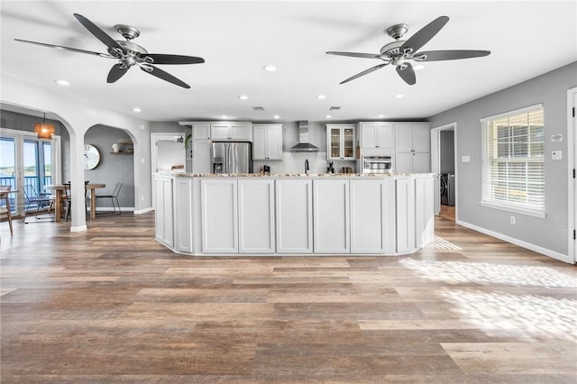 kitchen with wall chimney exhaust hood, a wealth of natural light, light wood-type flooring, and appliances with stainless steel finishes