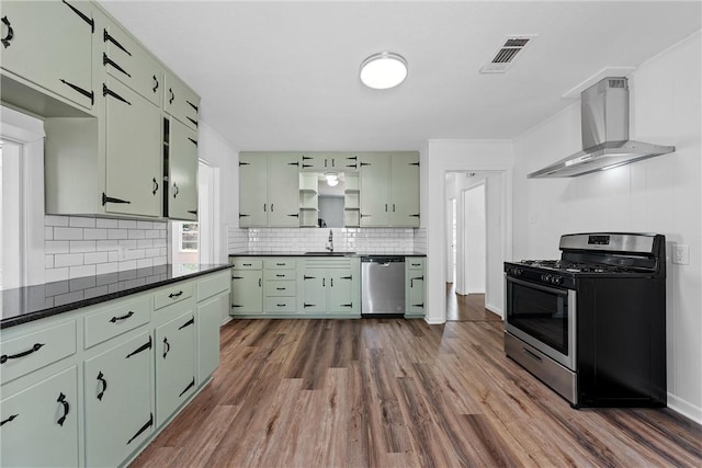 kitchen featuring dark wood-type flooring, green cabinets, wall chimney range hood, sink, and appliances with stainless steel finishes