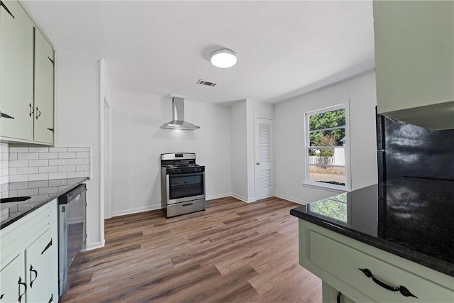 kitchen with backsplash, wall chimney exhaust hood, dark stone countertops, wood-type flooring, and stainless steel appliances