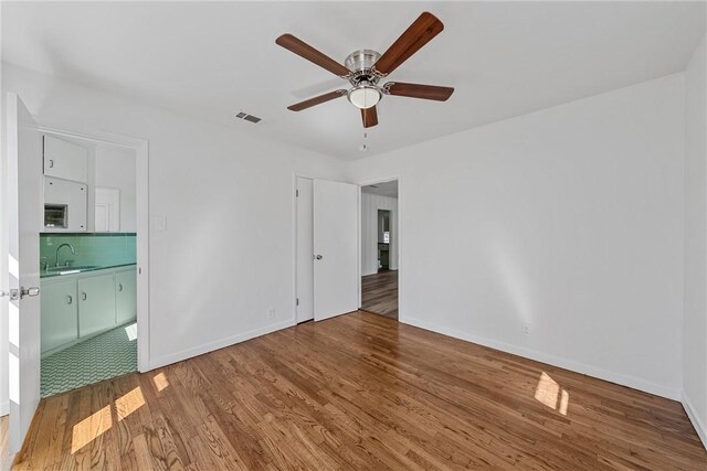 unfurnished bedroom featuring hardwood / wood-style floors, ceiling fan, and sink