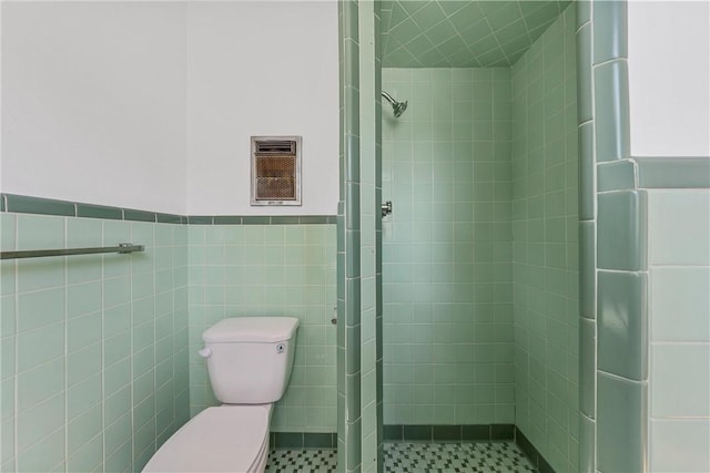 bathroom with a tile shower, toilet, and tile walls