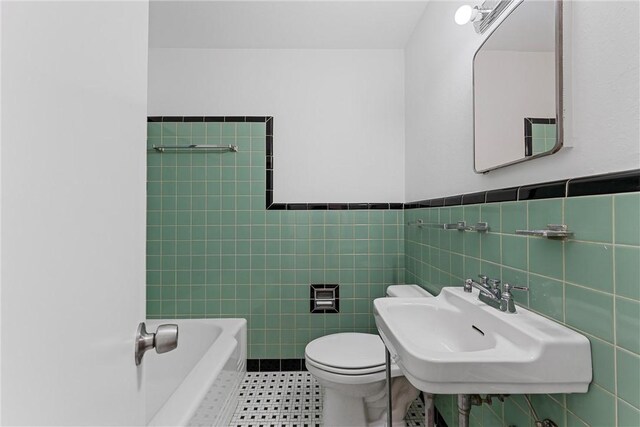 bathroom with a bathtub, toilet, tile walls, and sink