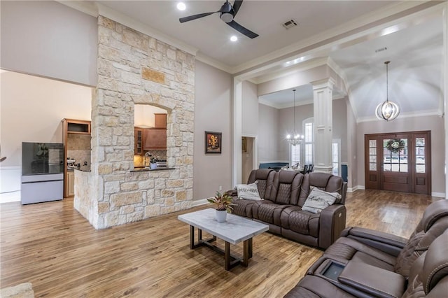 living room featuring a high ceiling, ceiling fan with notable chandelier, ornamental molding, light hardwood / wood-style floors, and decorative columns