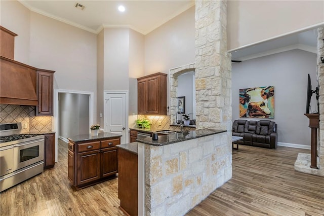 kitchen with backsplash, kitchen peninsula, dark stone countertops, range with two ovens, and ornamental molding