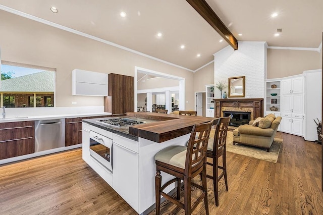 kitchen featuring lofted ceiling with beams, a large fireplace, stainless steel appliances, light hardwood / wood-style floors, and white cabinets