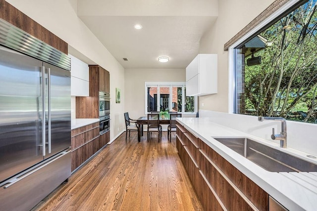 kitchen with sink, high end refrigerator, hardwood / wood-style floors, and white cabinets