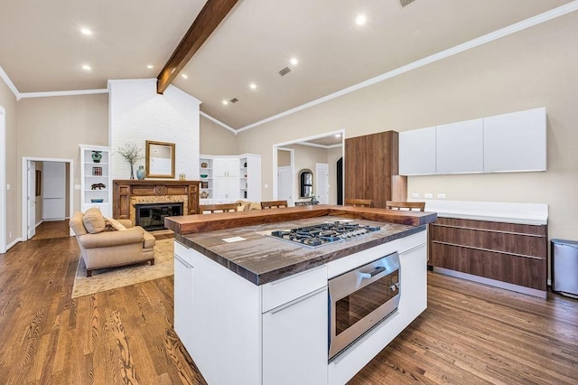 kitchen featuring beamed ceiling, a large fireplace, white cabinets, a kitchen island, and stainless steel gas stovetop