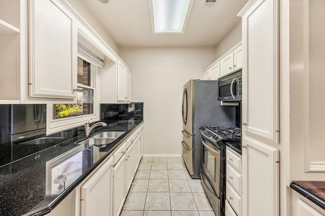 kitchen featuring sink, light tile patterned floors, stainless steel appliances, white cabinets, and dark stone counters