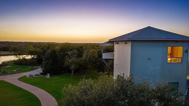 property exterior at dusk with a lawn and a water view