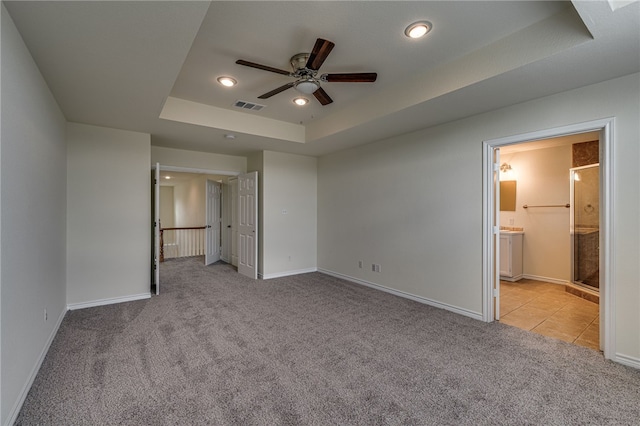 unfurnished bedroom featuring ensuite bathroom, ceiling fan, light colored carpet, and a tray ceiling