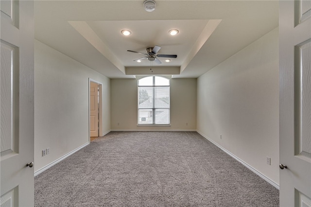 empty room with a tray ceiling, ceiling fan, and light colored carpet