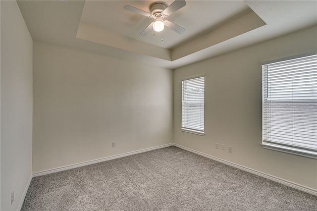 empty room with ceiling fan, a raised ceiling, and light colored carpet