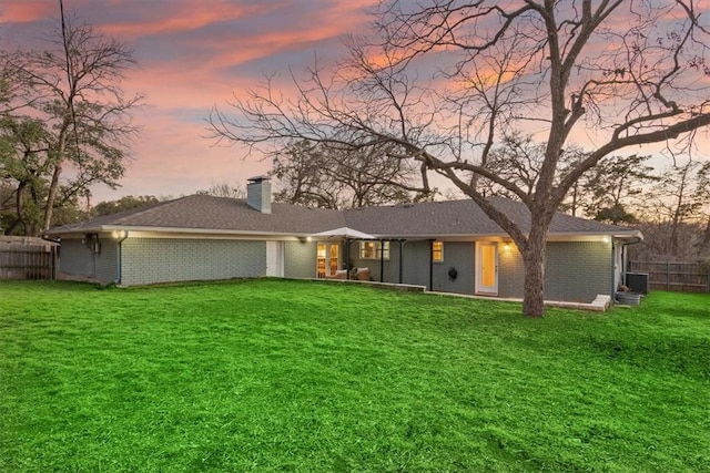 back of property at dusk featuring a yard, a chimney, fence, and brick siding