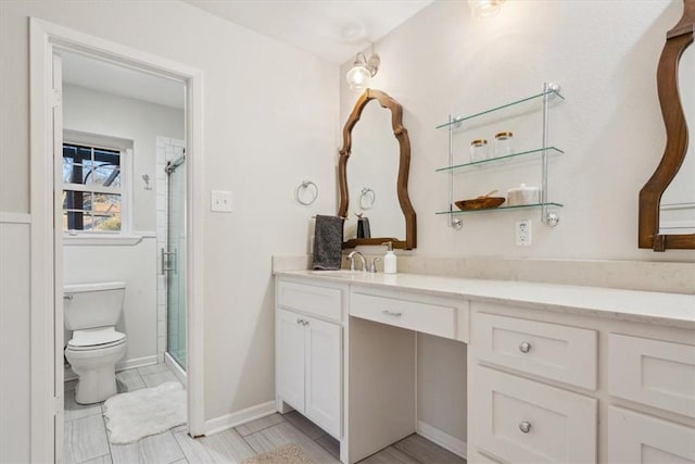 bathroom featuring toilet, a stall shower, baseboards, and vanity