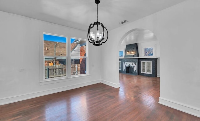 unfurnished dining area with a fireplace, dark hardwood / wood-style flooring, ornamental molding, and an inviting chandelier