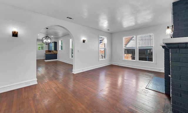 unfurnished living room with plenty of natural light, an inviting chandelier, dark hardwood / wood-style flooring, and a brick fireplace