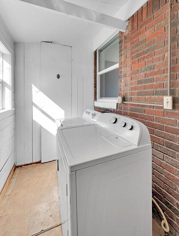 clothes washing area featuring separate washer and dryer and brick wall