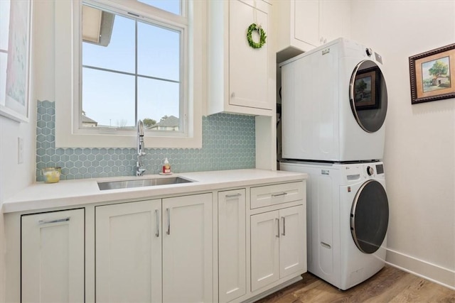 laundry area featuring sink, cabinets, light wood-type flooring, and stacked washer and clothes dryer