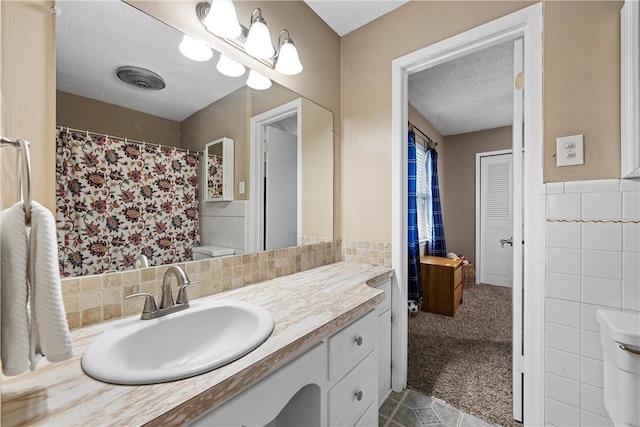 bathroom with vanity, a textured ceiling, toilet, and tile walls