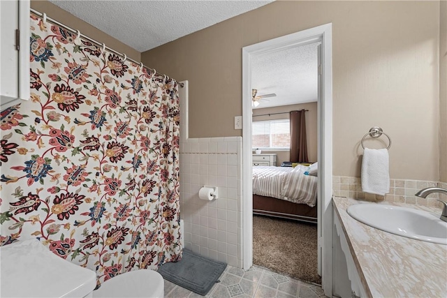 bathroom featuring tile walls, vanity, ceiling fan, toilet, and a textured ceiling