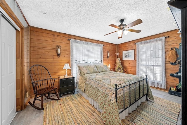 bedroom with ceiling fan, light wood-type flooring, wooden walls, and a closet