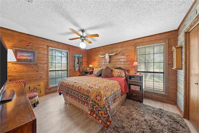 bedroom featuring light wood-type flooring, ceiling fan, and wooden walls