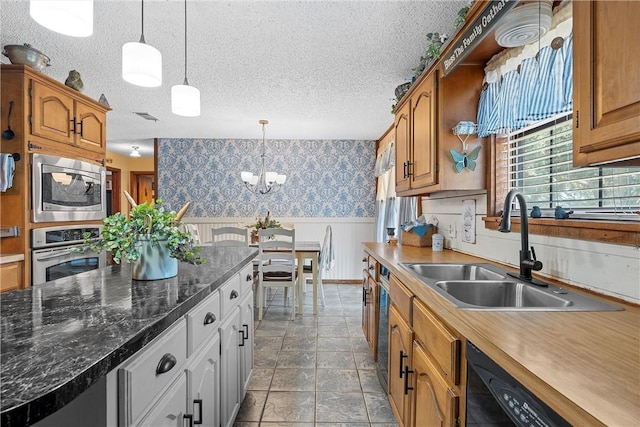 kitchen with sink, pendant lighting, a textured ceiling, and appliances with stainless steel finishes