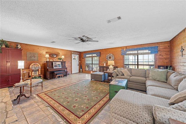 living room featuring ceiling fan, wooden walls, and a textured ceiling