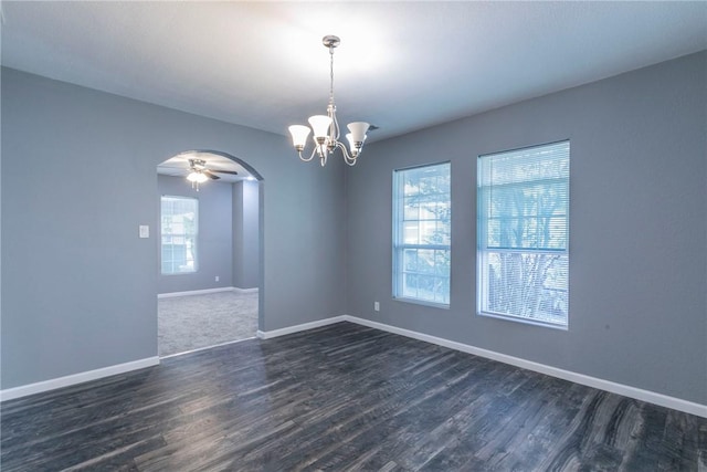 empty room featuring ceiling fan with notable chandelier, a healthy amount of sunlight, and dark wood-type flooring