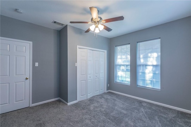 unfurnished bedroom with ceiling fan, dark carpet, a closet, and multiple windows