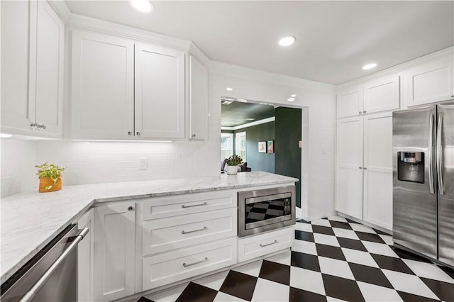 kitchen with white cabinetry, appliances with stainless steel finishes, light stone countertops, and decorative backsplash