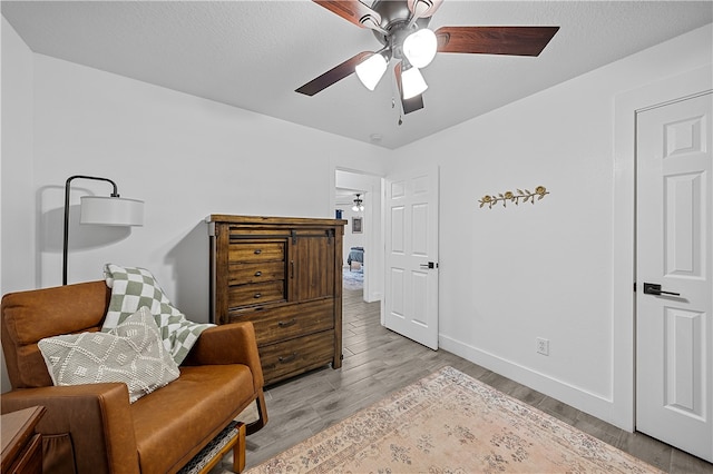 living area with a textured ceiling, light wood-type flooring, and ceiling fan