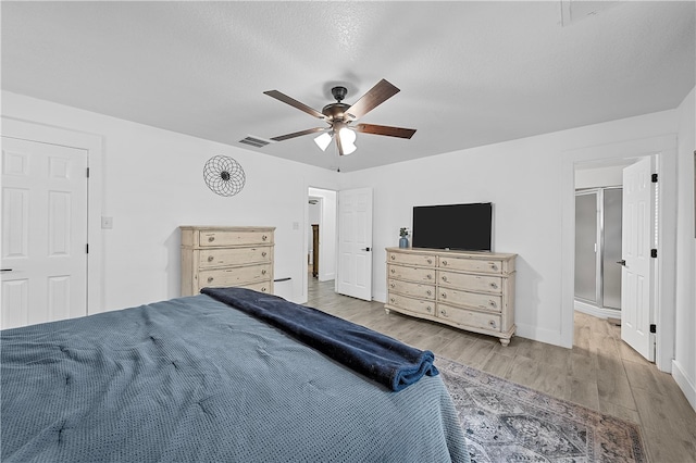 bedroom featuring ceiling fan, ensuite bath, a textured ceiling, and light hardwood / wood-style flooring