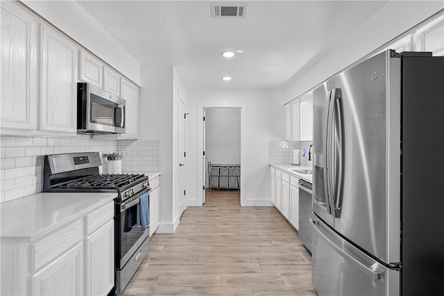 kitchen featuring white cabinetry, stainless steel appliances, backsplash, a textured ceiling, and light wood-type flooring