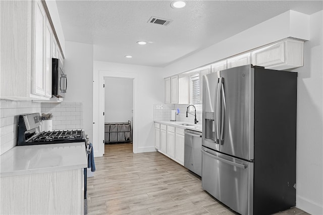 kitchen featuring backsplash, white cabinetry, stainless steel appliances, and light hardwood / wood-style floors