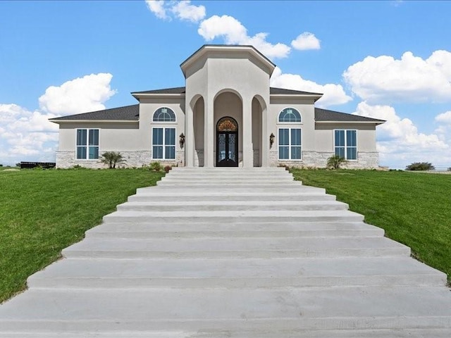 view of front facade with stone siding, a front yard, french doors, and stucco siding