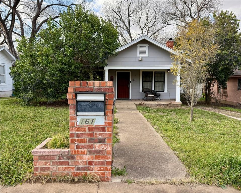 bungalow-style home with covered porch, a chimney, and a front yard