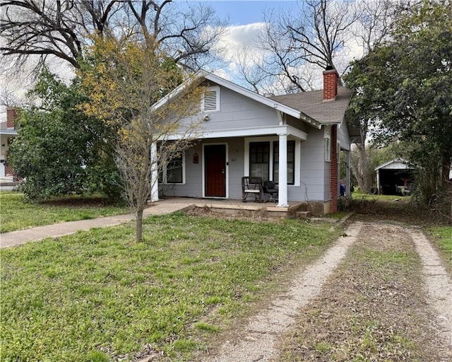 bungalow-style home with a porch, a front yard, a chimney, and dirt driveway