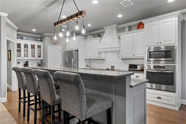 kitchen featuring a center island with sink, white cabinets, and custom exhaust hood