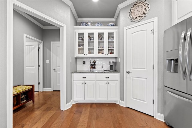 bar featuring light wood-type flooring, backsplash, crown molding, white cabinets, and stainless steel fridge with ice dispenser