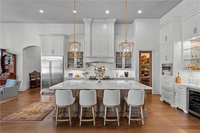 kitchen featuring built in appliances, a center island with sink, and hanging light fixtures